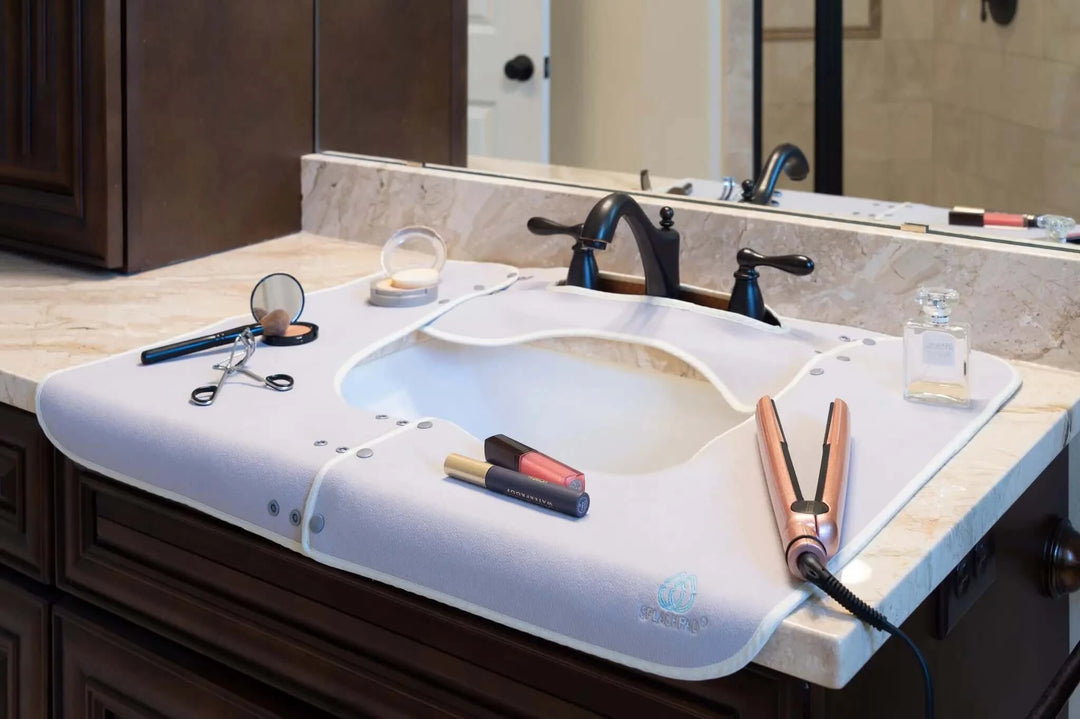 Grey Splashpad with Makeup and Hot Tools Protecting a Marble Bathroom Sink Countertop and Faucet
